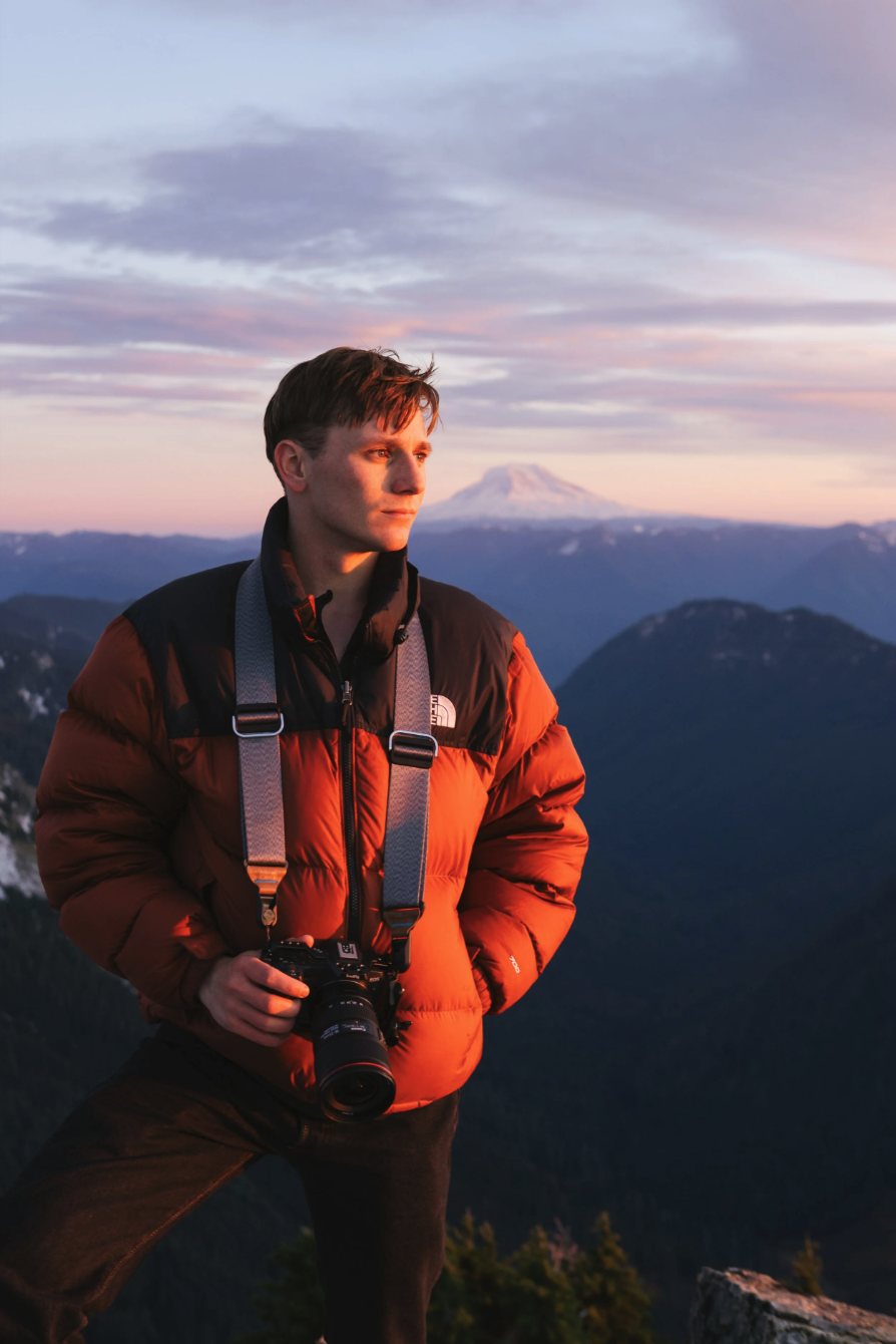 Mitchell Ellero with a camera at sunset, Mount Rainier behind him